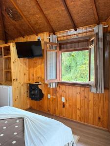 a bedroom with a bed and a tv and a window at Chales Vale da Nascente in Monte Verde