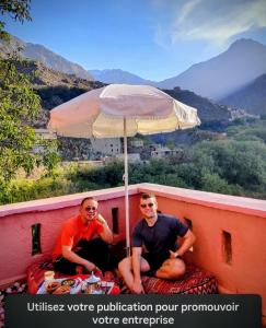 two men sitting on a ledge under an umbrella at Atlas Rooftop Imlil in Imlil