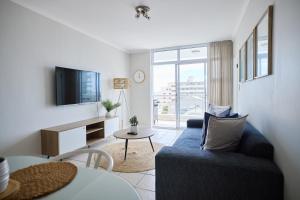 a living room with a blue couch and a tv at 2 Bedroom Bloubergstrand Apartment with Ocean Views in Bloubergstrand