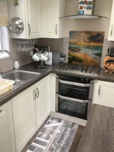 a kitchen with white cabinets and a stove and a sink at Home from Home in Eyemouth