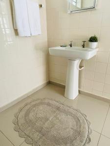 a white bathroom with a sink and a rug at Hotel Pousada La Vierro in Ponta Grossa