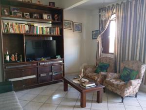 a living room with a tv and two chairs and a coffee table at Férias pé na areia, sol e mar in Serra