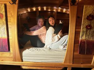 Zwei Frauen sitzen mit Büchern in einem Etagenbett. in der Unterkunft Bitty Bunky in Nelson