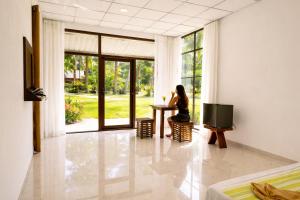 a woman sitting at a table in a room with a window at Cottage Paramount in Udawalawe