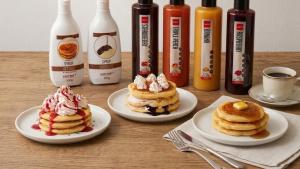 three plates of pancakes on a table with bottles of syrup at レックスインなんば in Osaka