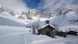 a small building in the snow with a mountain at Rododendro Apartment in Passo San Pellegrino