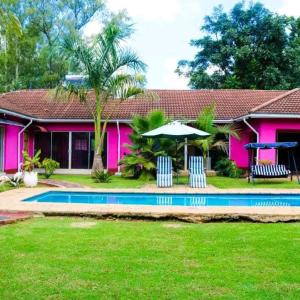 a pink house with a pool and a table and umbrella at Niyonest Guesthouse in Harare
