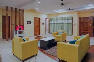 a living room with yellow chairs and a table at Prana pulse villa stay gokulam in Mysore