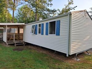 a white tiny house with blue windows and a porch at Camping Les Peupliers in Saint-Père-en-Retz