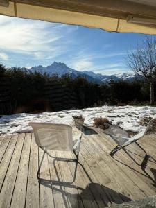 two chairs sitting on a wooden deck with snow at Petite chambre à la montagne in Ollon