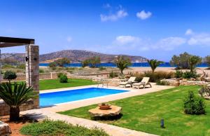 a backyard with a swimming pool and a lawn with chairs at Muses Beach Villas - Urania in Sitia