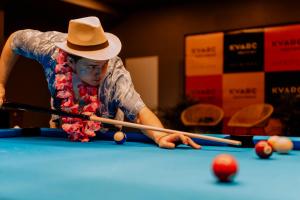 a man in a hat playing pool on a pool table at KVARC Hotel in Valmiermuiža