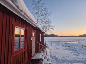 a cabin in the snow next to a frozen lake at Sjöstugan in Leksand