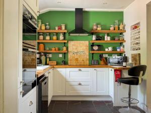 a kitchen with green walls and white cabinets at Foresters Cottage, Dalry in Dalry