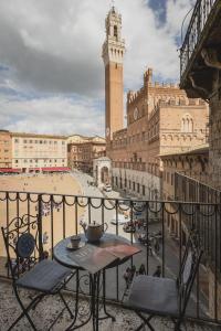a table and chairs on a balcony with a clock tower at Residenza d'Epoca " Il Campo" by FrancigenaApartments in Siena