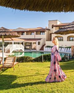 a woman in a dress walking in the grass in front of a house at Hotel Sa Pedra in Murta Maria