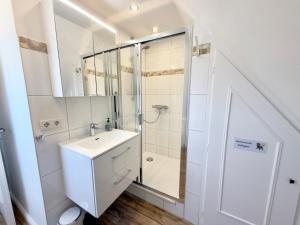 a white bathroom with a shower and a sink at Westerheide 51, App 1 in Wenningstedt +12 photos