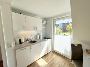 a kitchen with white cabinets and a large window at Westerheide 51, App 2 in Wenningstedt