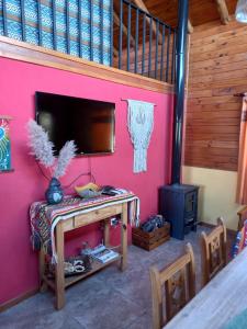 a room with a pink wall with a table and a stove at CABAÑAS ALMA SERENA in Capilla del Monte