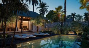 a pool with lounge chairs and a house with palm trees at Sandesh Water Edge Kabini in Begūr