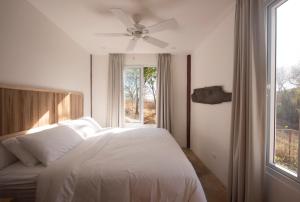 a bedroom with a bed with a ceiling fan and a window at Tropical Design Stay near Playa Avellanas with Rooftop Terraces in Santa Cruz