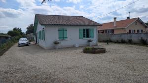 a small white house with green windows on a gravel driveway at Marychris in Saint-Loubès