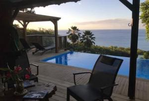 a patio with a pool and chairs and the ocean at Villa Vigie in Deshaies