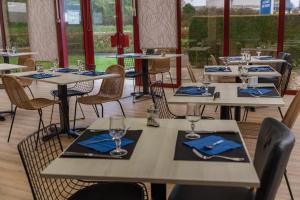 a row of tables in a restaurant with blue napkins at Brit Hotel Argentan in Argentan