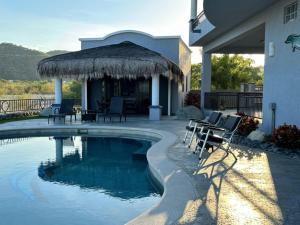 a swimming pool with chairs and a straw umbrella at Sunny Poolside Escape Near the Beach in Los Barriles