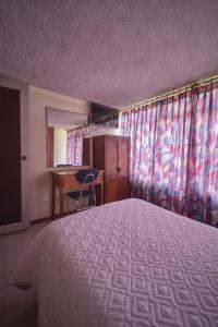 ein Schlafzimmer mit Bett, Schreibtisch und Vorhängen in der Unterkunft Hotel Los Alamos in Riobamba