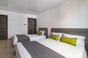 two beds in a hotel room with yellow pillows at Hotel Exito La 21 in Pereira
