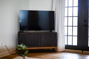 a flat screen tv on a wooden stand in a room with two windows at Golf Course Views, Sunsets & Chill Vibes in Columbus