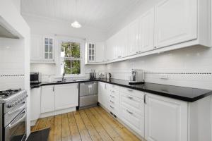 a white kitchen with white cabinets and black counter tops at Poets Cottage c1912 Scenic Hikes, Fire, Spa Bath in Wentworth Falls