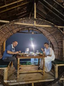 two men sitting at a table in a wicker room at Aadharjun Homestay in Chidām