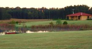 a field with a house and a boat on a lake at Broken View Estate in Pokolbin