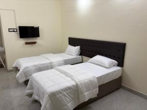 two beds in a room with a tv on the wall at Balaas Inn in Karaikal
