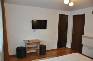 a room with a bed and a table and a tv on the wall at Pensiunea La Ionica in Dâmbovicioara