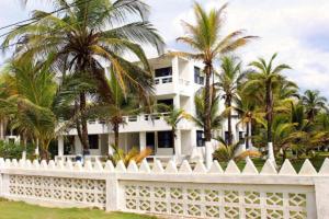 a white house with palm trees behind a white fence at Apartamentos Las Múcuras in Coveñas +10 photos