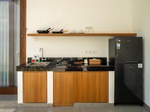 a kitchen with a sink and a black refrigerator at Prawara Uluwatu in Uluwatu