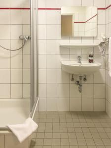 a white tiled bathroom with a sink and a shower at Hotel Salina B&B - mit Parkplatz, Zentral und Digital in Bad Rothenfelde