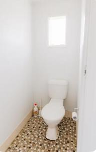 a white toilet in a bathroom with a tiled floor at Bungo Beach Shack in Eden +10 photos