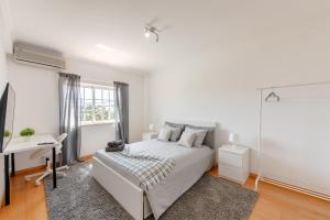 a white bedroom with a bed and a desk at Lisbon Coastal Retreat in Charneca