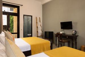 a hotel room with two beds and a desk and a television at Divulgaha Gedara Boutique Hotel in Anuradhapura