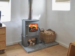 a wood stove in a room with a basket of logs at Granny Mcphees Cottage Hssh in Beaworthy