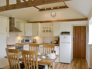 a kitchen with white cabinets and a wooden table and chairs at The Stables in Occold
