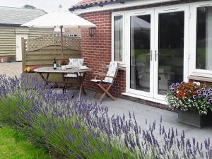 a patio with a table and an umbrella and some flowers at Holly Lodge in Hemsby +18 photos