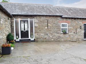 a stone house with a black door and a window at Sgubor Llwyndu in Bettws