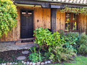 a wooden house with a black door and some plants at Bockety Barn in Stalham