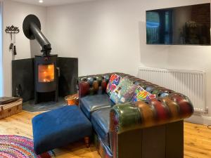 a living room with a leather couch and a fireplace at Carreg Gwenlais Barn in Carmel