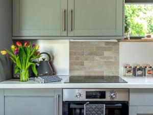 a kitchen with green cabinets and a vase of flowers at Meadow Hide - Uk36773 in Chichester